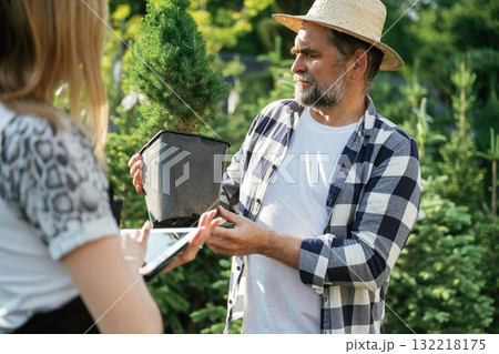 Taking a plant in a pot. Woman and man are working in the garden together with plants 132218175