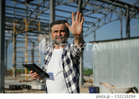 Giving orders by the hand. Senior worker is near the unfinished greenhouse, working Giving orders by the hand. Senior worker is near the unfinished greenhouse, working 132218204