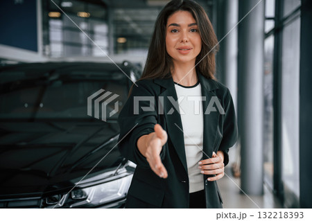 Giving a hand to shake, making a deal. Saleswoman in car showroom, selling automobile Giving a hand to shake, making a deal. Saleswoman in car showroom, selling automobile 132218393