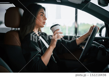 White cup of fresh drink in hand. Beautiful businesswoman is in the new car White cup of fresh drink in hand. Beautiful businesswoman is in the new car 132218436