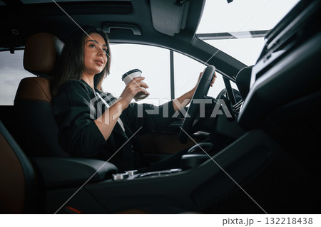 White cup of fresh drink in hand. Beautiful businesswoman is in the new car White cup of fresh drink in hand. Beautiful businesswoman is in the new car 132218438