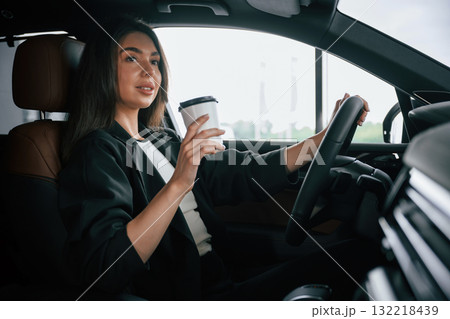 White cup of fresh drink in hand. Beautiful businesswoman is in the new car 132218439
