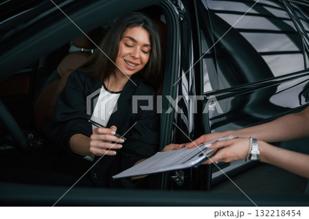 Writing by a pen. Process of buying new car, woman is signing documents while sitting in a new automobile 132218454