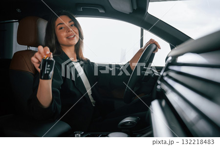 Black colored keys of new automobile. Beautiful businesswoman is in the new car Black colored keys of new automobile. Beautiful businesswoman is in the new car 132218483