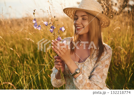Holding plant and smiling. Beautiful young woman is on the field, countryside Holding plant and smiling. Beautiful young woman is on the field, countryside 132218774