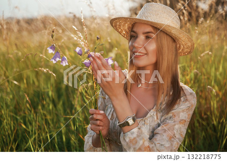 In straw hat, with plant in hands. Beautiful young woman is on the field, countryside 132218775