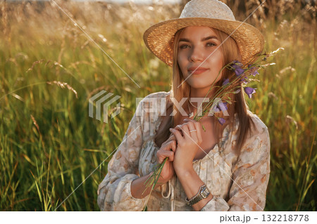 In straw hat, with plant in hands. Beautiful young woman is on the field, countryside 132218778