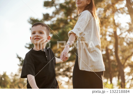 Holding each other by a hands. Mother and son are in the forest together Holding each other by a hands. Mother and son are in the forest together 132218884