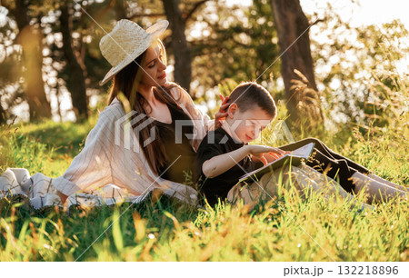 Sitting and reading the book. Mother and son are in the forest together 132218896