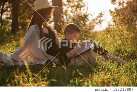 Sitting and reading the book. Mother and son are in the forest together Sitting and reading the book. Mother and son are in the forest together 132218897