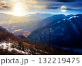 mountainous countryside on spring equinox. day and night time change concept. winter to spring season change scenery. melting snow and leafless trees on the rolling hills with sun and moon 132219475