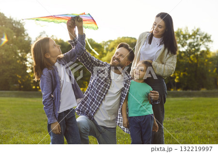 Happy smiling young family flying colorful kite in park and enjoying leisure activity outdoors. Happy smiling young family flying colorful kite in park and enjoying leisure activity outdoors. 132219997