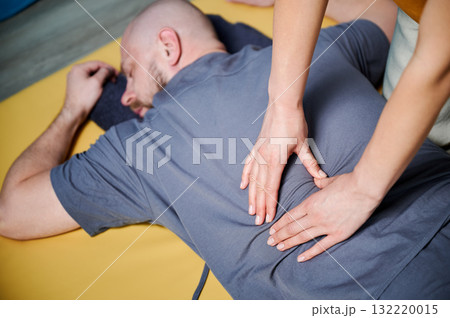 Masseuse making thai yoga massage. Therapist doing traditional massage treatment for male patient indoors. Bald client lying on mat, meditating, enjoying hand massage in calm atmosphere. 132220015
