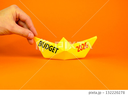 Budget 2026 symbol. Concept words Budget 2026 on beautiful yellow paper boat. Beautiful orange paper background. Businessman's hand. Business and budget 2026 concept. Copy space. Budget 2026 symbol. Concept words Budget 2026 on beautiful yellow paper boat. Beautiful orange paper background. Businessman's hand. Business and budget 2026 concept. Copy space. 132220278