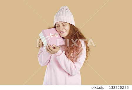 Happy young woman in warm pastel pink winter clothes holding gift box and smiling 132220286