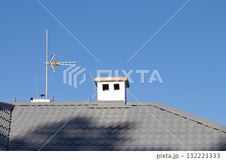 Chimney and antenna on a sloped roof under a clear blue sky at midday 132221333