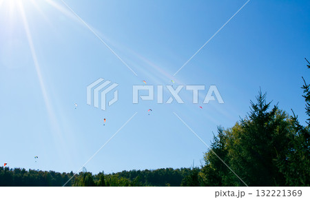 Paragliders soaring high above a blue sky and lush green trees on a sunny day 132221369
