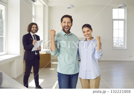 Young smiling family couple happy about buying a new apartment standing with man realtor. Young smiling family couple happy about buying a new apartment standing with man realtor. 132221808