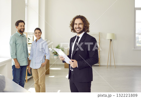 Young man realtor standing with happy couple looking at camera in new house. 132221809