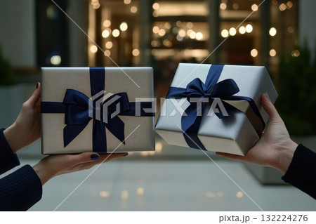 Elegant gift boxes with dark ribbons held by two individuals in a festive setting 132224276
