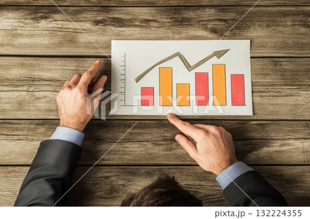 Businessman in Suit Pointing at Bar Graph Displaying Positive Growth on Wooden Table 132224355