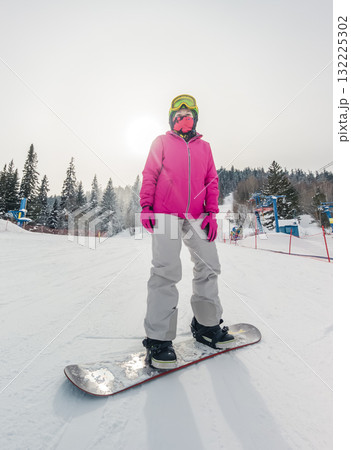 A snowboarder stands on a snowy slope, dressed in a vibrant pink jacket and goggles 132225302