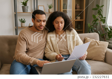 Young african american couple managing finances together on sofa with laptop and papers. concept of budgeting, household expenses, financial planning 132227631