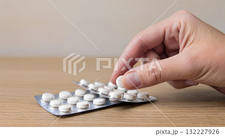 A hand takes a white pill from a blister pack. Concept of treatment and pharmacology. A hand takes a white pill from a blister pack. Concept of treatment and pharmacology. 132227926