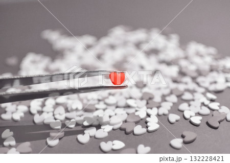 ピンセットで摘まんだハート型のトッピングシュガー　おしゃれでかわいい背景装飾　気持ち　心象風景 132228421