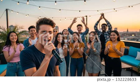 Young caucasian man singing at rooftop party with friends during sunset, celebrating friendship and summer fun. concept of music, social gathering, joyful expression Young caucasian man singing at rooftop party with friends during sunset, celebrating friendship and summer fun. concept of music, social gathering, joyful expression 132228633
