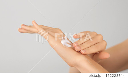 Close-up of female hands applying moisturizing cream on neutral background. Hygiene, Body care, and Skincare concept.  132228744
