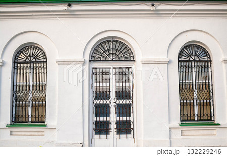 Architectural facade featuring arched windows and decorative ironwork on a white building exterior Architectural facade featuring arched windows and decorative ironwork on a white building exterior 132229246
