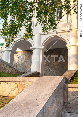 Architectural details of stone steps leading to arched columns under a leafy tree canopy 132229258