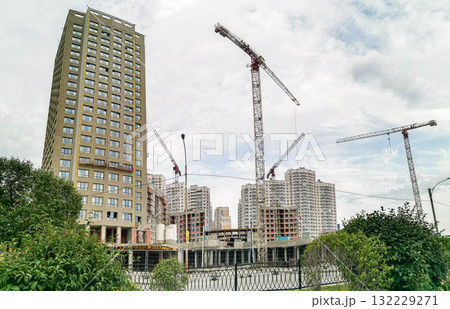 Modern residential building under construction with cranes and greenery in urban environment 132229271