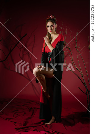 Woman poses gracefully in traditional Japanese dress against a striking red backdrop 132229758