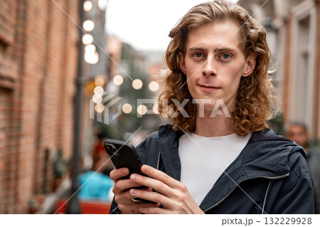 Young man using smartphone in a lively street with warm lights at dusk Young man using smartphone in a lively street with warm lights at dusk 132229928