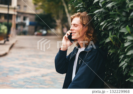 Young man talking on the phone in a quiet urban park on a sunny day Young man talking on the phone in a quiet urban park on a sunny day 132229968