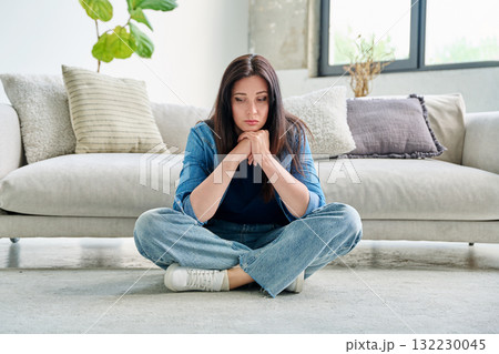 Sad upset young woman with sitting on floor near sofa at home Sad upset young woman with sitting on floor near sofa at home 132230045