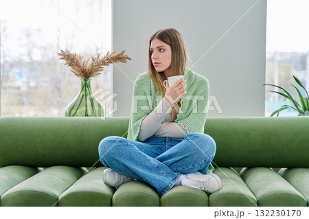 Portrait of relaxed beautiful young woman sitting at home on sofa with cup 132230170