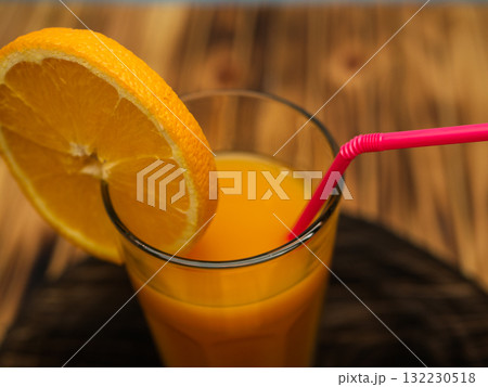Full glass of orange juice close-up. Fresh orange juice on wooden table in out of focus unidentified restaurant in the morning in summer. 132230518