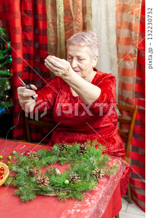 Cut with scissors. Senior old woman craft. Grandmother make Christmas wreath from pine branches. Home decoration in December. Winter Holiday preparing 132230732