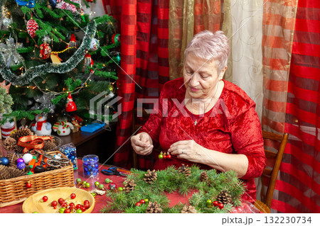 Senior old woman crafting. Grandmother make Christmas wreath from pine branches. Home decoration in December. Winter Holiday preparing Senior old woman crafting. Grandmother make Christmas wreath from pine branches. Home decoration in December. Winter Holiday preparing 132230734