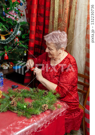 Portrait of senior old woman craft. Grandmother make Christmas wreath from pine branches. Home decoration in December. Winter Holiday preparing. DIY 132230736