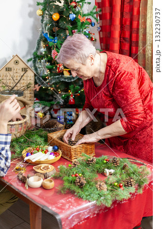 Senior old woman craft. Grandmother make Christmas wreath from pine branches. Home decoration in December. Winter Holiday preparing 132230737