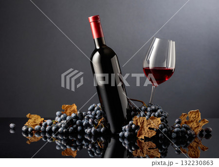 Bottle and glass of red wine with blue grapes on a black background. Bottle and glass of red wine with blue grapes on a black background. 132230863