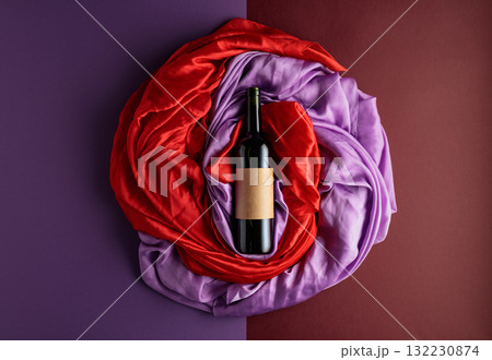 Bottle of red wine against a background of draped red and purple silk fabric. 132230874