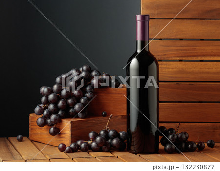 Bottle of red wine and blue grapes on a wooden background. 132230877