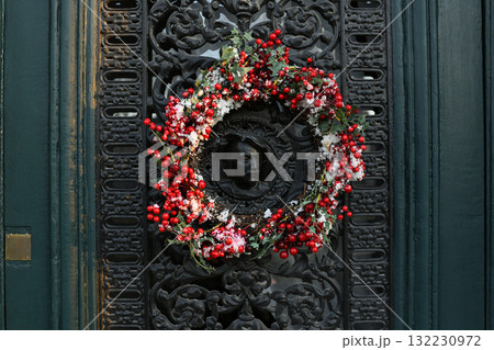 A Christmas wreath of red berries on a metal door with a bas-relief portrait of a man 132230972