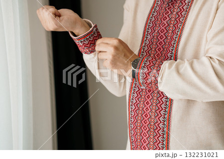 Man Dressing Traditional Embroidered Vyshyvanka Shirt. Close-Up. Cream Fabric. Red Geometric Patterns. Ukrainian Culture. Authentic Style. Preparation. 132231021