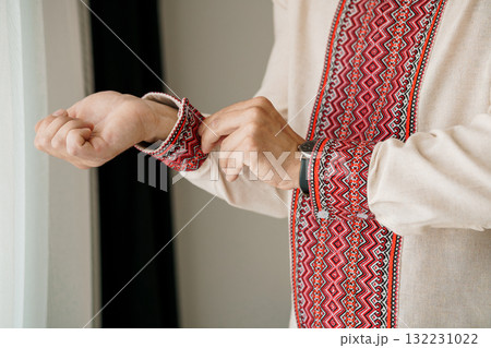 Man Adjusting Embroidered Shirt Cuff with Watch, Traditional Ukrainian Vyshyvanka, Natural Light, Beige and Red Textile Detail, Cultural Fashion. Man Adjusting Embroidered Shirt Cuff with Watch, Traditional Ukrainian Vyshyvanka, Natural Light, Beige and Red Textile Detail, Cultural Fashion. 132231022